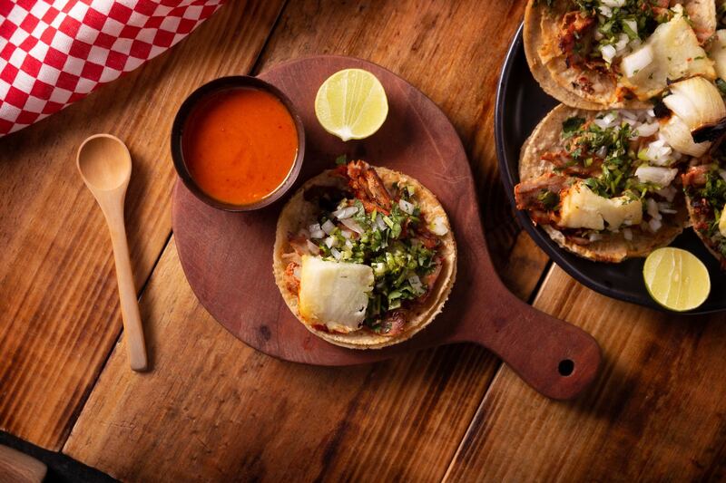 Tacos al pastor servidos en tabla de madera con limón y salsa