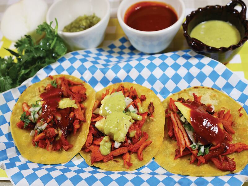 Tres tacos al pastor con salsa verde sobre papel de cuadros