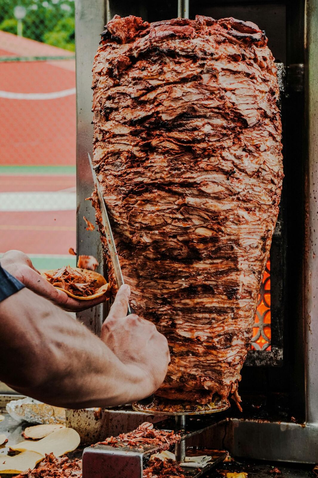 Trompo de pastor girando frente a la brasa mientras se rebana la carne